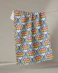The Renee Fly "70s Floral" recycled kitchen towel, featuring vibrant retro shapes in yellow, orange, pink, and blue, hangs on a string against a neutral background.