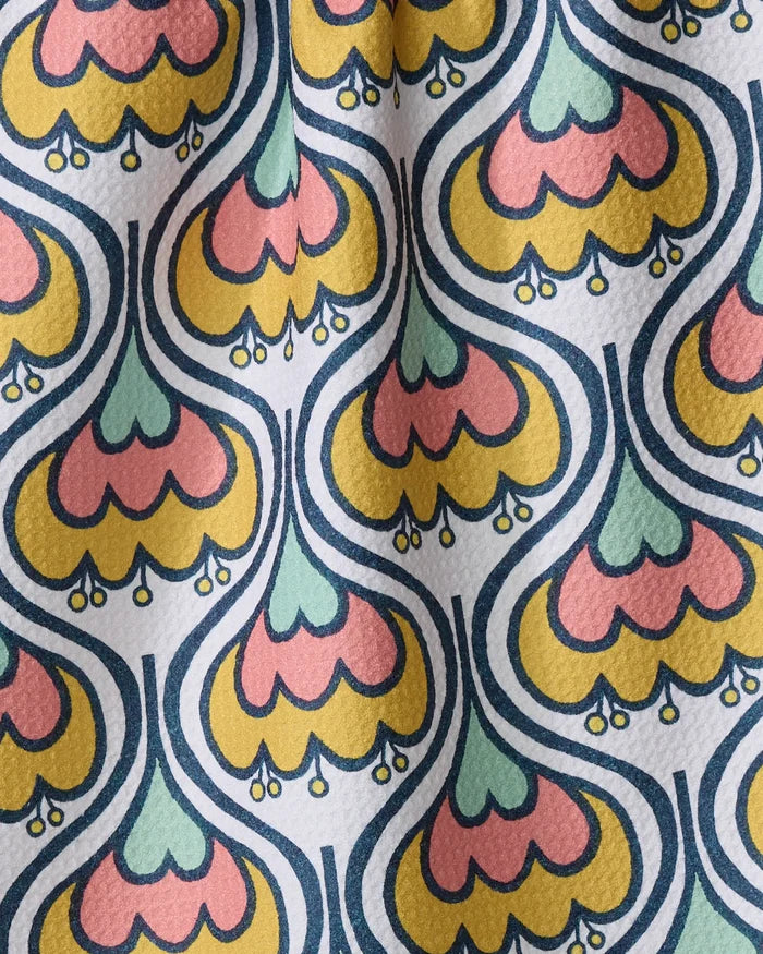 The Renee Fly 70s Floral kitchen towel features a colorful, retro-style pattern with yellow, pink, and teal petals outlined in blue on textured white recycled fabric.