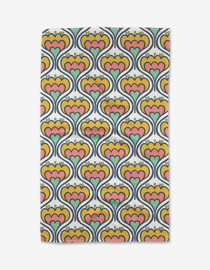 The Renee Fly 70s Floral tea towel features a rectangular shape with a retro floral pattern of heart-shaped orange, green, and pink flowers outlined in navy on a yellow background.