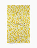 The A Bunch of Bananas Tea Towel by Geometry features a repeating yellow banana pattern on a light Geoweave fabric, shown slightly wrinkled against a plain white background.