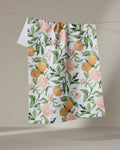 The "A Peony For Your Thoughts" recycled kitchen towel by Aubrey Fairchild, with a vibrant floral and foliage pattern, hangs on a line against a plain beige background.
