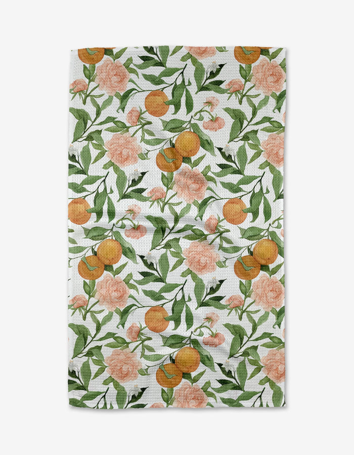 Aubrey Fairchild’s “A Peony For Your Thoughts” tea towel features a vibrant pattern of oranges, green leaves, and pink flowers on white Geoweave™ fabric.