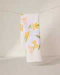 The GEOMETRY Abloom tea towel, made from ultra-absorbent recycled materials, features a white background with yellow, orange, and purple flowers and green leaves—perfect for brightening any kitchen.