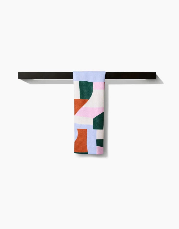 The Claire Iglesias Abstract Collage Bar Towel features bold geometric shapes in green, red, blue, pink, and white. Made from Geoweave fabric, it hangs neatly on a black rod against a plain white background for style and function.