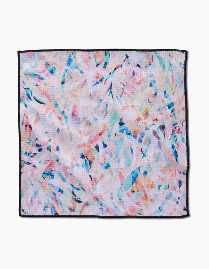 The Rachel Parker Abstract Jungle napkin is a square cloth made from ultra-absorbent Geoweave fabric, featuring a pastel pink, blue, peach, and white abstract pattern with sleek black edging.