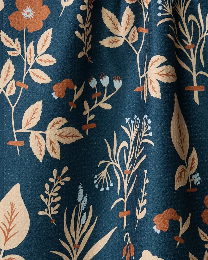 The Aemilius by Danelys Sidron is a dark blue recycled kitchen towel with a vintage botanical pattern of beige, tan, and light blue leaves, flowers, and stems.