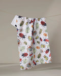 The "African Beetles" recycled kitchen towel by Taryn Brennan, featuring colorful beetle illustrations, hangs on a clothesline against a neutral backdrop.
