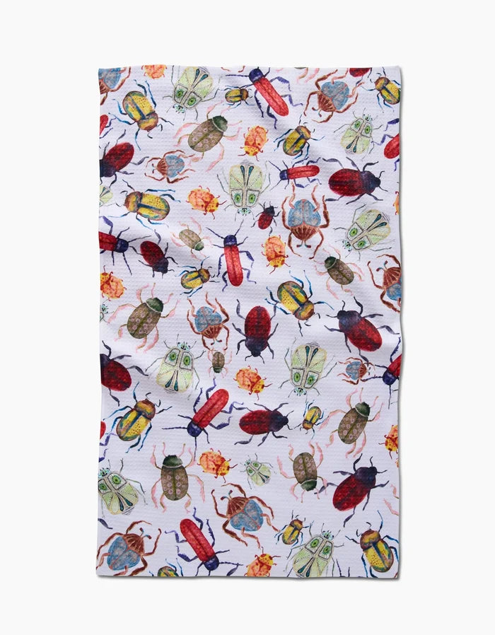 The African Beetles tea towel by Taryn Brennan features a colorful, scattered pattern of illustrated beetles, moths, and insects in red, green, yellow, and blue on white Geoweave fabric with a slightly wrinkled look.