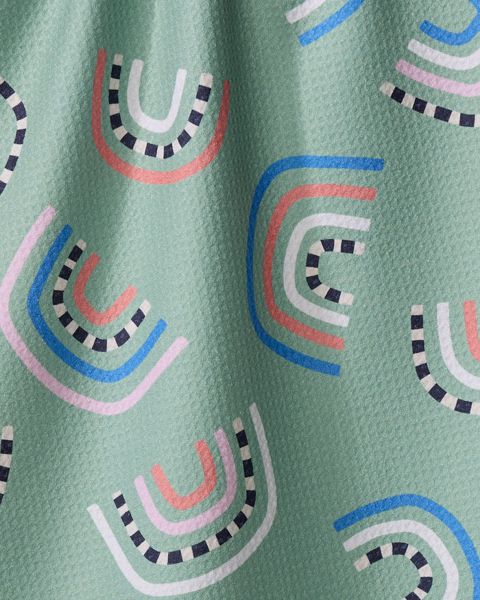 The After the Rain kitchen towel by Claire Iglesias is light green and textured, made from recycled materials, and features playful abstract rainbow-like shapes in pink, blue, red, white, and black with outlined details.