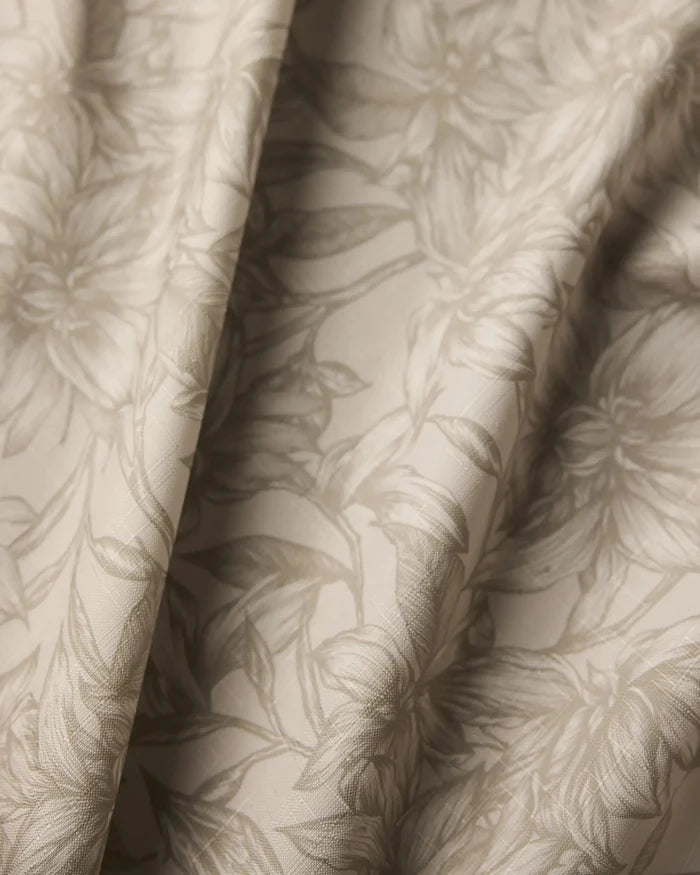 Close-up of Geometry’s Alba tablecloth fabric in beige, featuring a subtle floral pattern. The stain-resistant material is softly draped, forming gentle folds and shadows across its detailed surface.