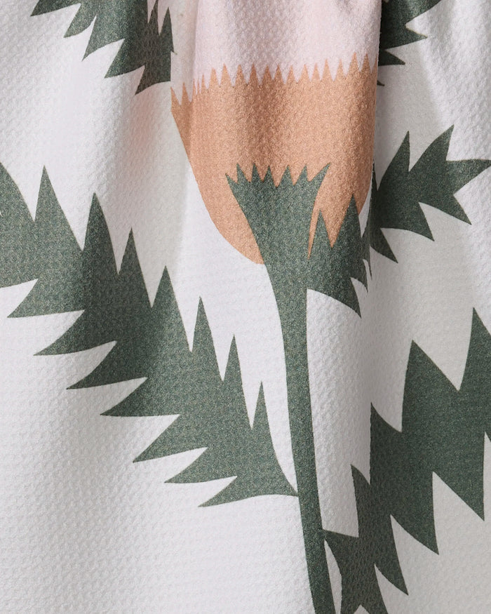 A close-up of the Along the Path recycled kitchen towel by Elana Gabrielle shows its absorbent, textured surface with a pink flower and jagged green leaves printed on a light background.
