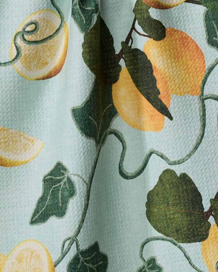 The Amalfi Lemons fabric by Pascale Dilger is made from recycled materials and features yellow lemons, green leaves, and twisting vines on a light blue textured background.