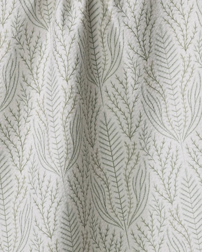 A close-up of the Amberlin tea towel by Amy MacCready, showcasing a subtle botanical design with delicate green leafy branches arranged vertically on a light background.