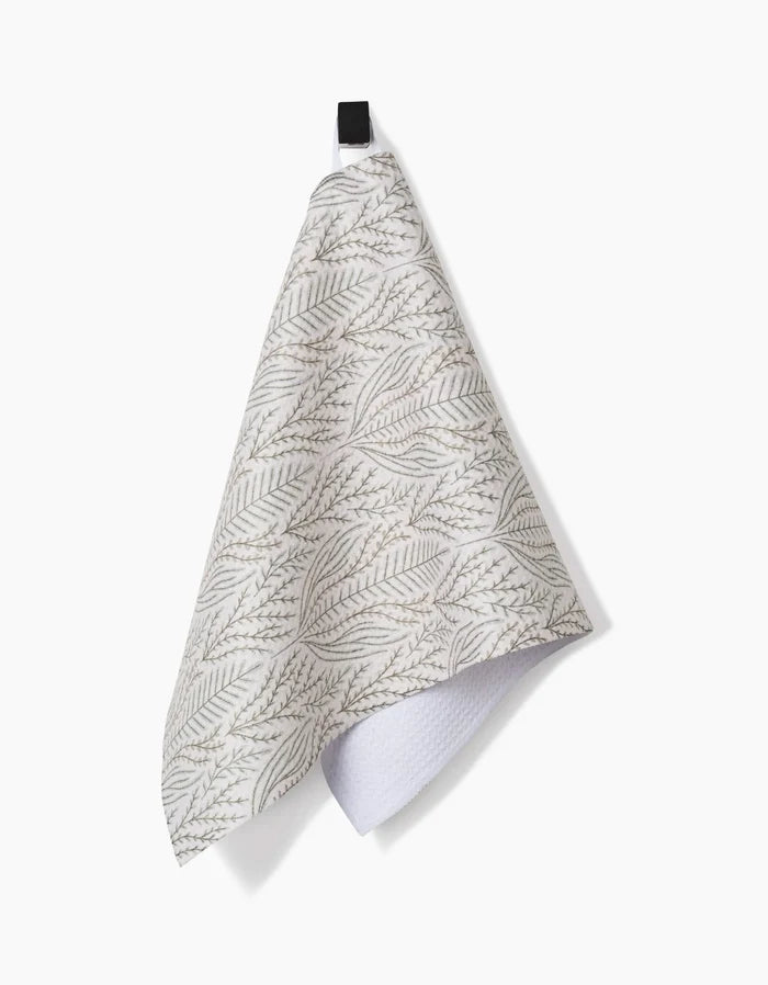 The Amy MacCready Amberlin Bar Towel features a gray leafy pattern and black loop, hangs against a white background. Ultra-absorbent with a folded corner showing its textured underside, it combines stylish design with practical function.