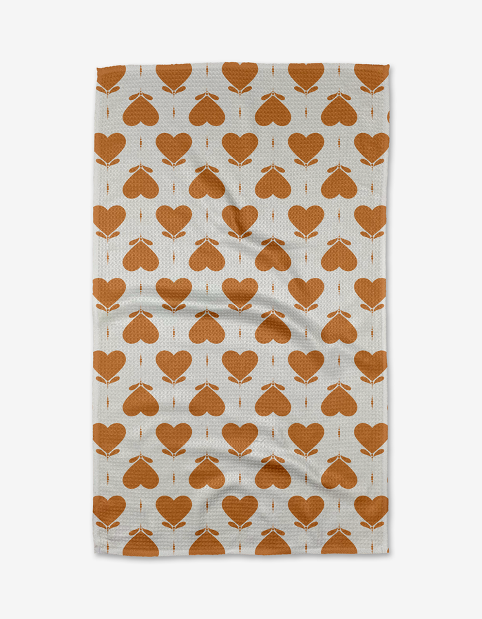 The Amor tea towel by Danelys Sidron features a repeating orange heart and arrow pattern in neat rows. Made from quick-drying recycled materials.