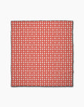 The Geometry Amorcito Gingham beach blanket features a red and white checkered grid with small hearts in each white square. Made from quick-drying recycled material, it’s outlined in black on a plain white background.