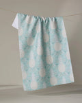 The Andre tea towel by Amy MacCready, featuring a light blue and white pineapple pattern and made from recycled materials, hangs over a clothesline against a plain, neutral background.