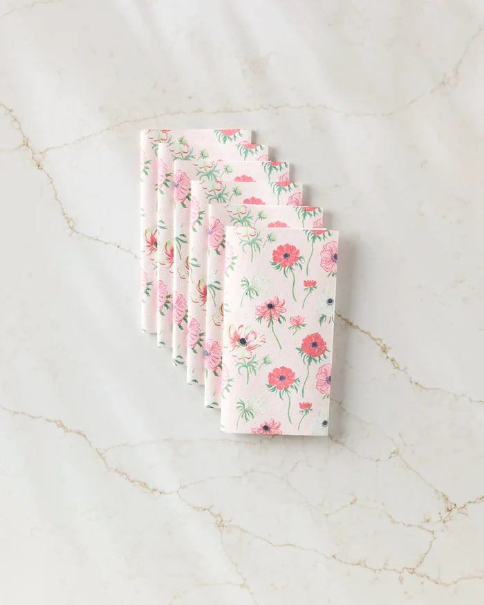 Six Anemone Garden Flowers napkins by Linda Fox, featuring a pink and green floral design on eco-friendly paper, are neatly fanned out on a marble surface.