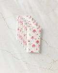 Six Anemone Garden Flowers napkins by Linda Fox, featuring a pink and green floral design on eco-friendly paper, are neatly fanned out on a marble surface.