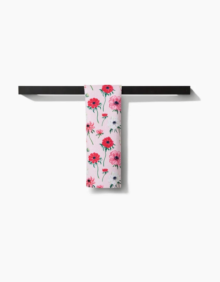 The Linda Fox Anemone Garden Flowers bar towel, featuring a pink and red floral design on white recycled fabric, hangs neatly over a simple black rack against a plain white background.