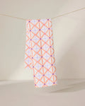 The GEOMETRY Anew tea towel features a quick-drying design with a pink and orange geometric crisscross pattern and small purple dots, shown hanging by a string against a neutral background.