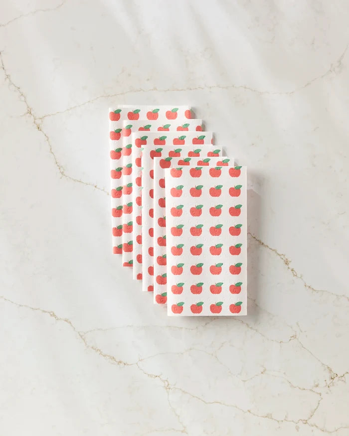 Five Apple Grove reusable paper towels by Brittany Jepsen, featuring small red apples and green leaves in a repeating pattern, are neatly folded and fanned out on a light marble surface.