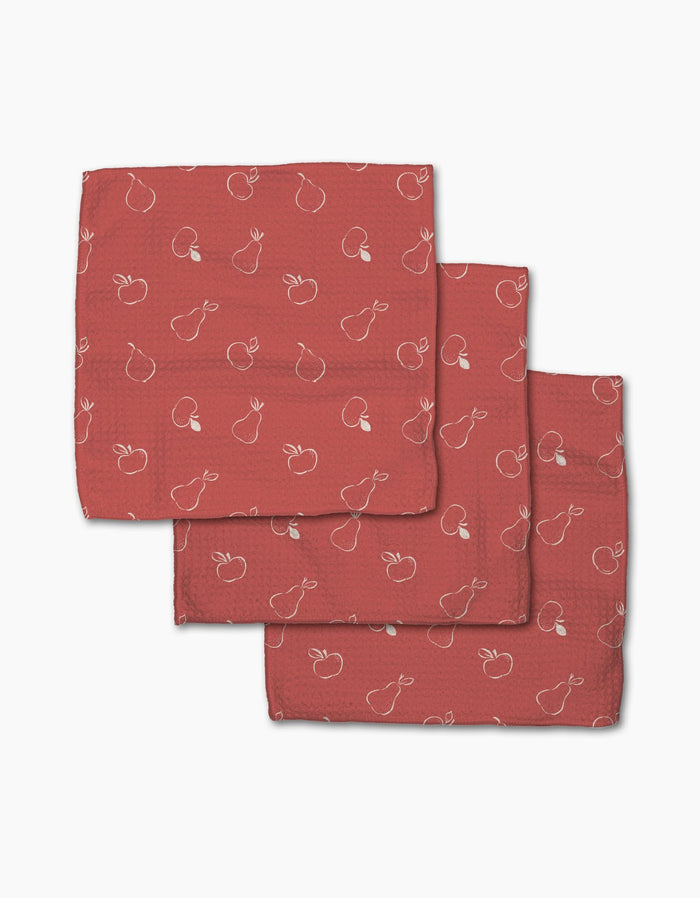 Three folded red cloth napkins from Linda Foxs Apples and Pears collection feature a subtle white outline pattern of apples and pears, made from recycled materials, displayed on a white background.