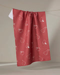 The Linda Fox "Apples and Pears" red tea towel, featuring a white outline pattern of apples and pears, hangs on a clothesline against a neutral background—perfect as a quick-drying kitchen towel.
