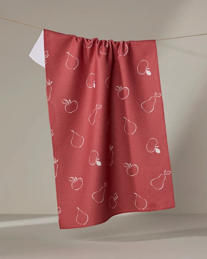 The Linda Fox "Apples and Pears" red tea towel, featuring a white outline pattern of apples and pears, hangs on a clothesline against a neutral background—perfect as a quick-drying kitchen towel.