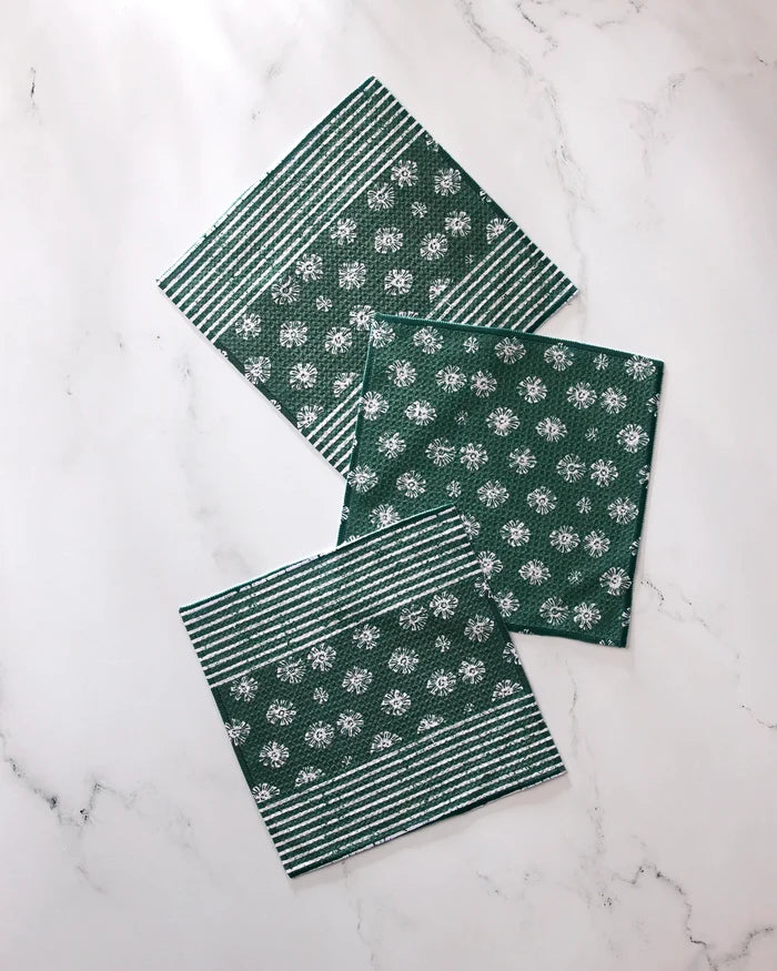 Three green Geometry Arbusto absorbent kitchen towels with white floral and stripe patterns are arranged on a white marble surface—two feature both stripes and flowers, while one displays only the floral design.