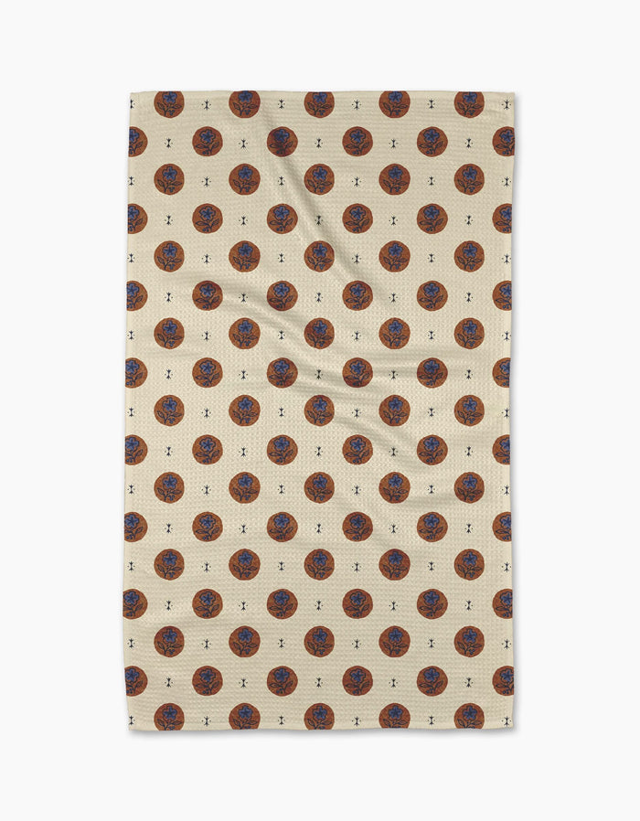 A beige Geometry Artisan Floral Tea Towel with a repeating pattern of red and blue circular floral designs and small black accents, displayed flat against a white background.
