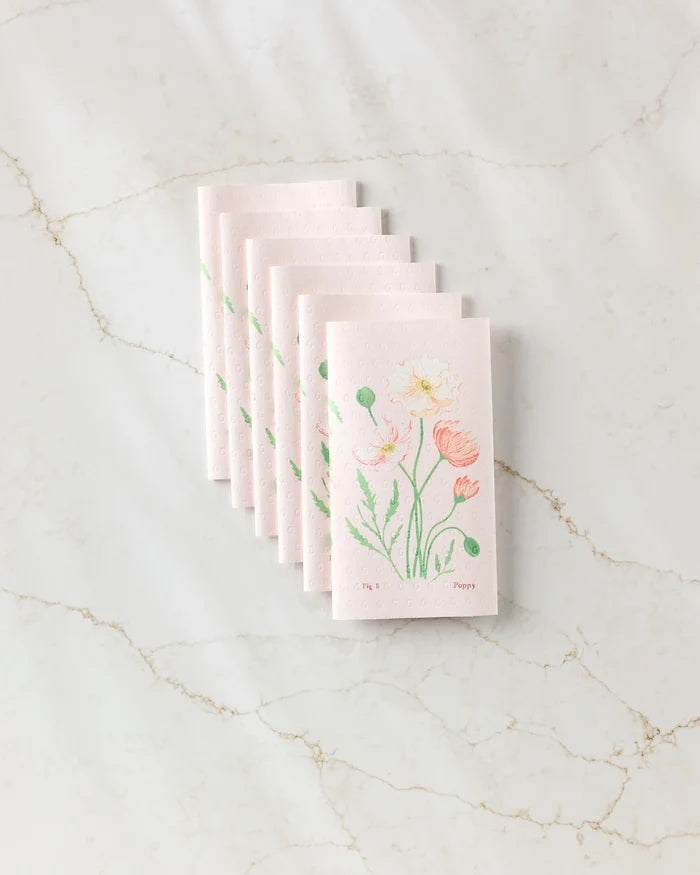 A stack of August Poppy seed paper cards by Linda Fox, adorned with hand-drawn pastel flowers and green leaves, rests on white marble—evoking the charm of eco-friendly, sustainable gifting.
