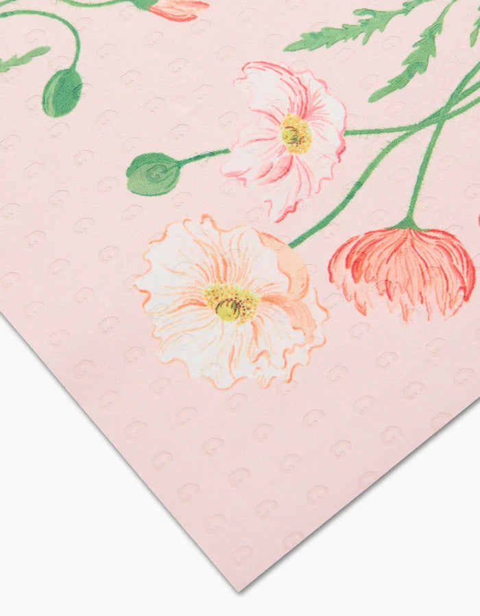 A close-up of August Poppy by Linda Fox—a pink sheet with red and white poppy illustrations and green leaves, made from eco-friendly post-consumer recycled materials. Small raised dots add subtle texture.