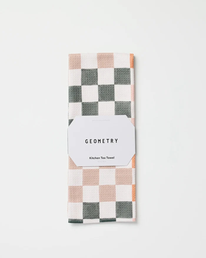 The GEOMETRY Autumn Checkers kitchen tea towel, featuring a white, gray, and light beige checkered pattern, is folded and wrapped with a white label reading "GEOMETRY Kitchen Tea Towel" on a white background.