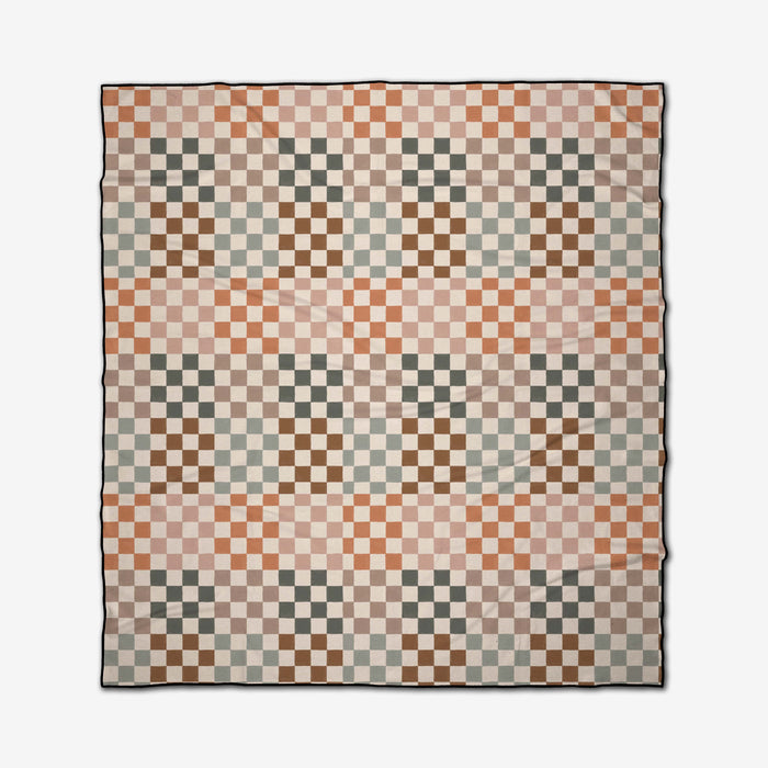The Autumn Checkers quilt by GEOMETRY features a checkerboard pattern of cream, brown, orange, and green squares arranged in diagonal waves, inspired by the Micro-loop Beach Blanket.