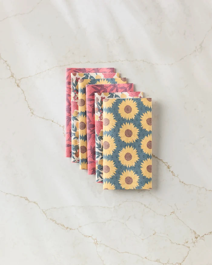 Four folded "Autumn Florals" reusable paper towels by Rebecca Bobko lay on a marble surface: two with a blue and yellow sunflower print, and two with a pink bird and flower pattern.