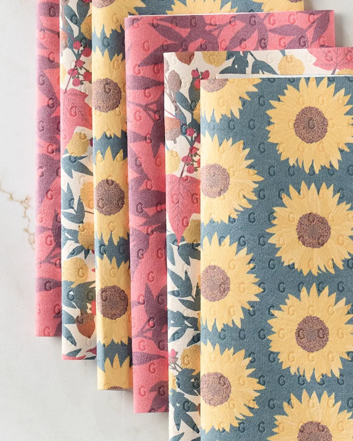Five folded Autumn Florals reusable paper towels by Rebecca Bobko are shown: two with large yellow sunflowers on blue, and three with pink/red florals on cream or pink backgrounds.
