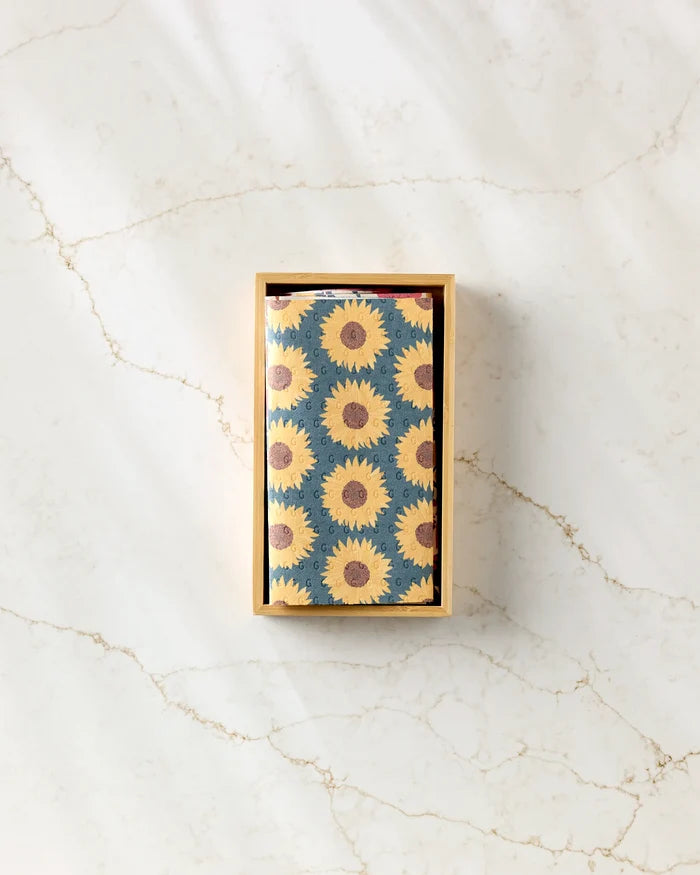 A rectangular box with a sunflower design, Autumn Florals by Rebecca Bobko, sits on a light marble surface with brown veining—ideal for storing eco-friendly paper towels.