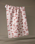 The Geometry Autumn Mushrooms tea towel, made from recycled materials and featuring a red mushroom and animal pattern, hangs on a string against a neutral background.