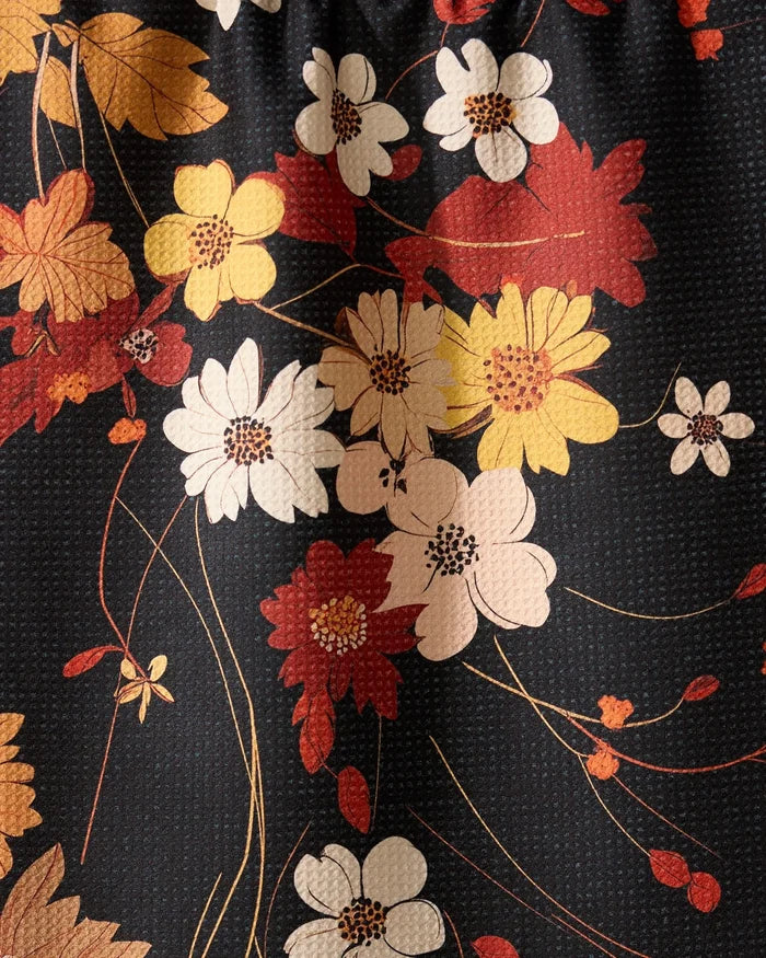 A close-up of the Geometry Autumn Whispers absorbent dish towel, showcasing its textured surface and a floral pattern with white, yellow, and red flowers plus green stems on a dark background.