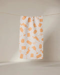 The GEOMETRY Bach Brunch bar towel is white, made from recycled materials, and features an orange hairdressing tool pattern. It hangs on a clothesline against a neutral background.