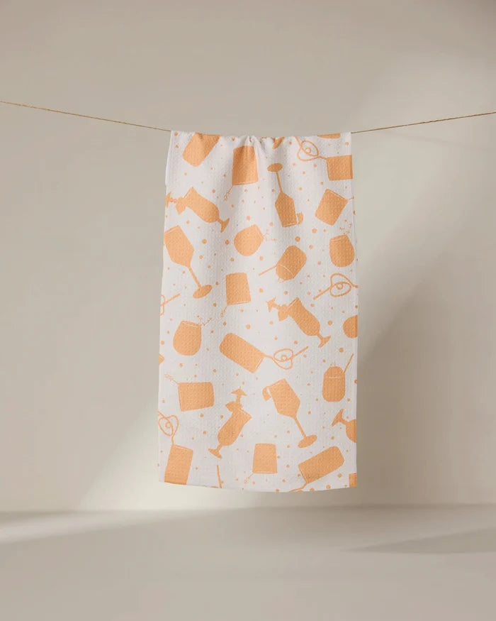 The GEOMETRY Bach Brunch bar towel is white, made from recycled materials, and features an orange hairdressing tool pattern. It hangs on a clothesline against a neutral background.