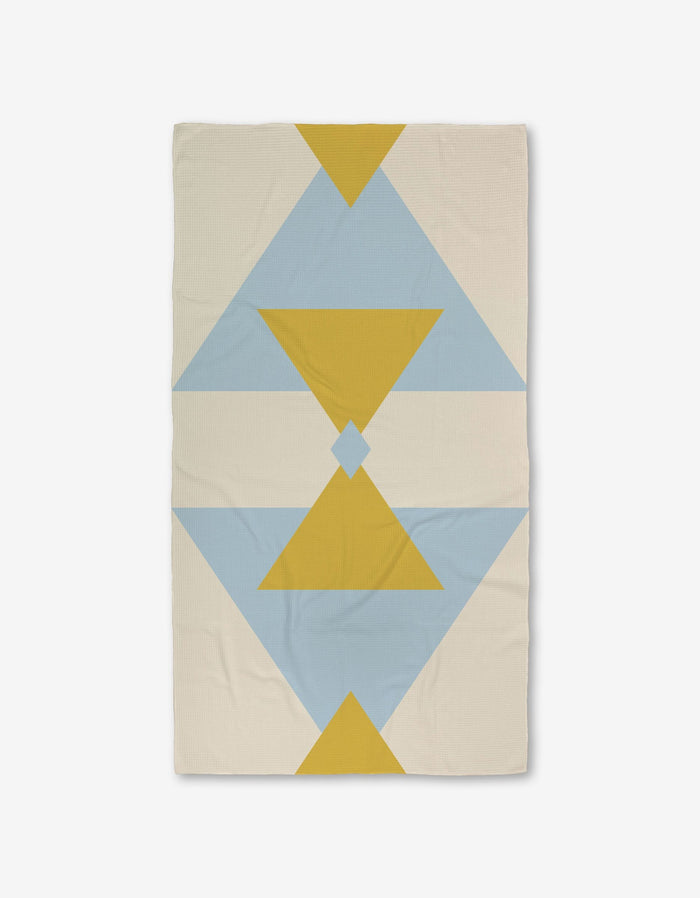 The GEOMETRY Balanced Blue blanket features a geometric pattern of yellow and blue triangles and diamonds on a cream background, with bold, symmetrical shapes running vertically. Made with ultra-absorbent Geoweave technology.