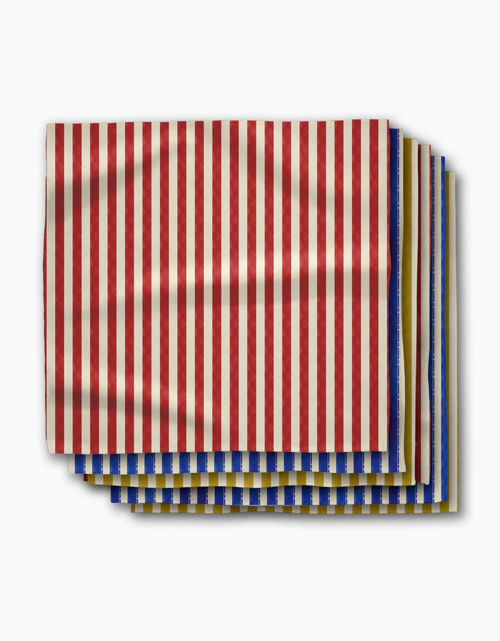 Geometrys Bauhaus Stripe dinner napkins, made from recycled materials, feature vertical red and beige stripes above layers with blue and yellow stripes, all displayed on a white background.