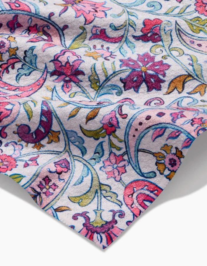 A close-up of the Bazaar bar towel by Maayan Alper-Swan, featuring ultra-absorbent Geoweave fabric with a vibrant floral and paisley pattern in pink, purple, blue, yellow, and green on a light background. The towel is slightly wrinkled at the edge.