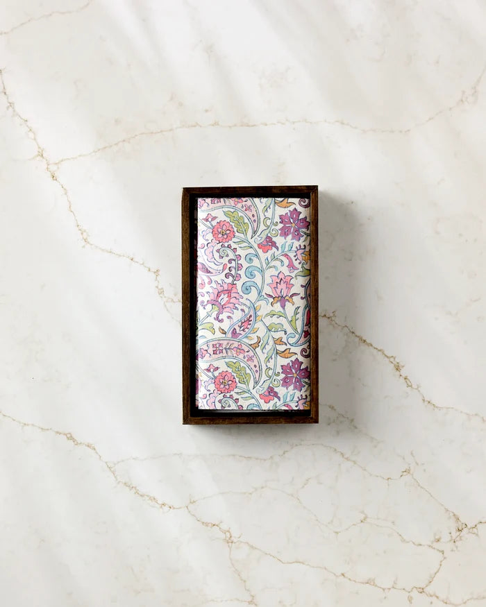 A rectangular box of Maayan Alper-Swan’s Bazaar kitchen towels with a floral-patterned lid in pink, purple, and green sits on a white marble surface with light brown veins.