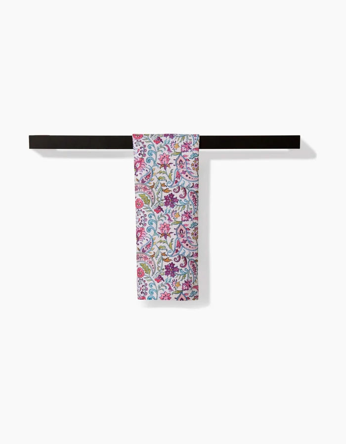 The Bazaar towel by Maayan Alper-Swan, featuring pink, yellow, and blue floral patterns, hangs neatly folded over a sleek black bar towel rack against a plain white background.