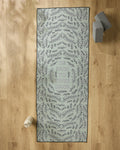 The Graphics and Grain "Be Kind To Your Mind" yoga mat with leafy patterns rests on a wooden floor, paired with a slip-resistant yoga towel, water bottle, and two stacked yoga blocks.