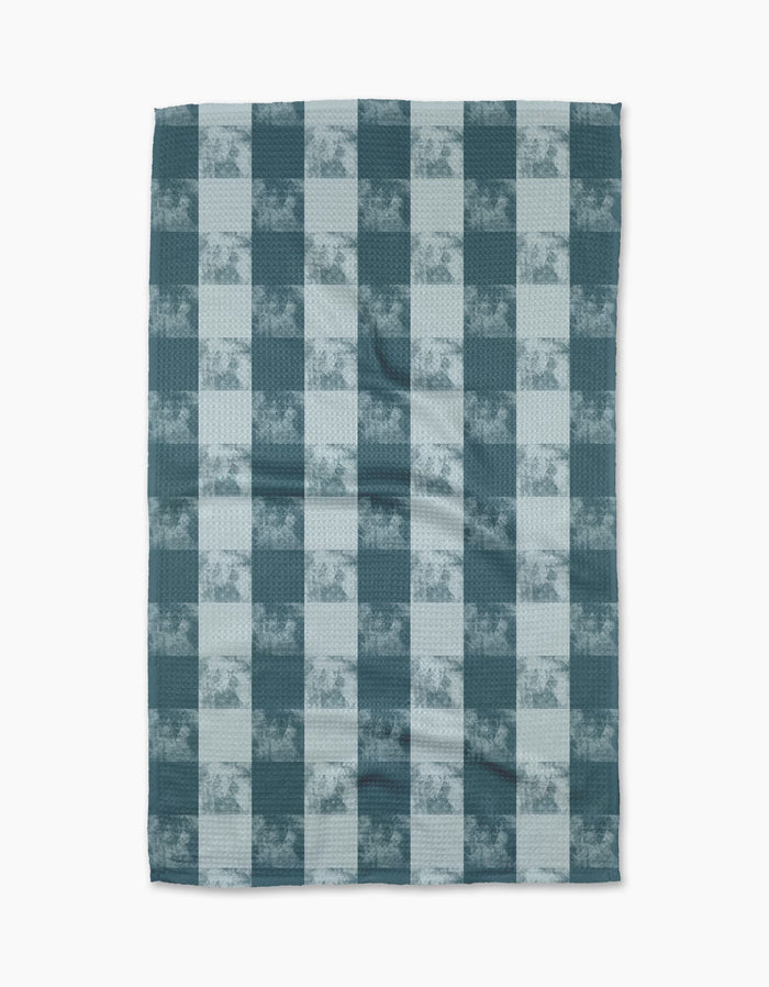 The Geometry “Beach Storm” blanket features a teal and light blue checkered pattern with subtle cherub accents on ultra-absorbent Geoweave™ fabric, creating a soft and cozy look ideal for relaxing moments.
