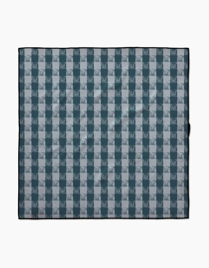 The Geometry Beach Storm blanket features a blue and white plaid pattern with alternating squares, a thin black border, and is made from recycled materials, shown laid flat on a white background.